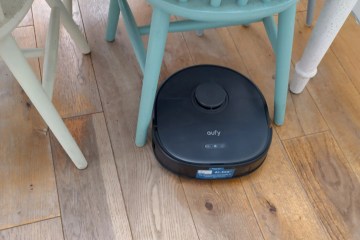 a black Eufy X10 Pro Omni robot vacuum cleaner is sitting on a wooden floor next to a chair