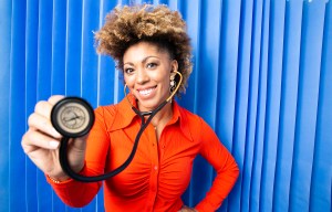 a woman in an orange shirt is holding a stethoscope in front of a blue curtain